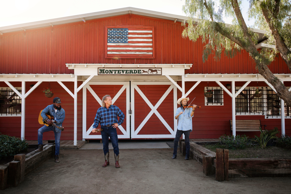 Three men performing music in front of red Monteverde barn