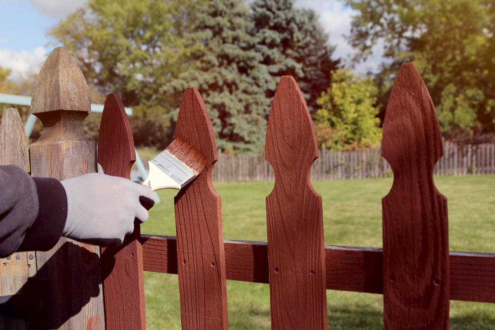 A man painting a wooden fence with a brush