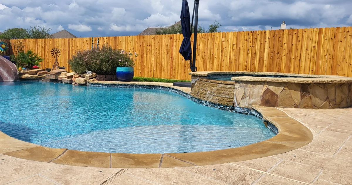 Completed Staining Projects 5 After fence staining Cypress TX showing beautiful cedar fence with golden stain finish surrounding luxury pool area with water slide, stone spa, and decorative landscaping in residential backyard