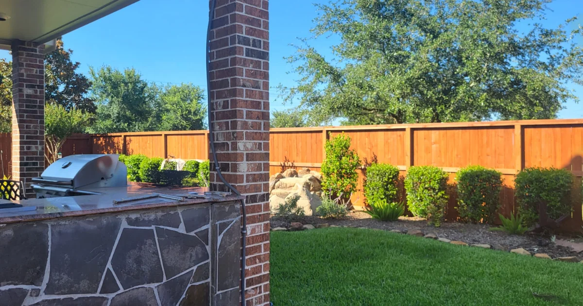 Completed Staining Projects 7 After fence staining in The Woodlands TX showing perfectly matched property line cedar fence with rich orange-brown Sherwin Williams stain finish enhancing backyard with outdoor kitchen, stone landscaping and lush green lawn