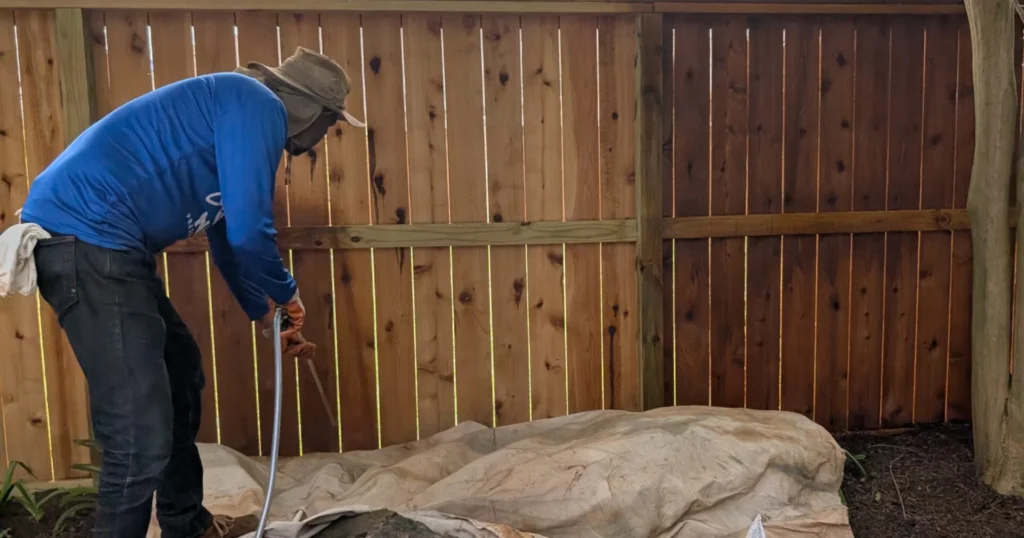 Professional fence stainer applying protective stain after watermark removal using spray equipment in Houston Texas