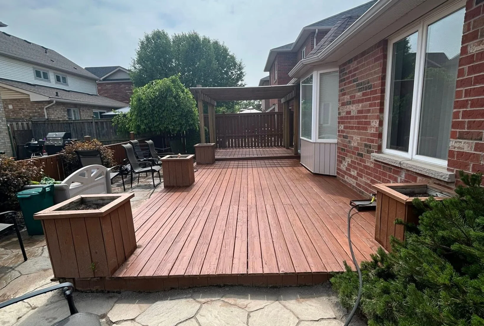 deck-staining-after-restoration-houston-backyard Beautifully restored backyard deck with rich cedar stain finish planters and pergola after professional deck staining service