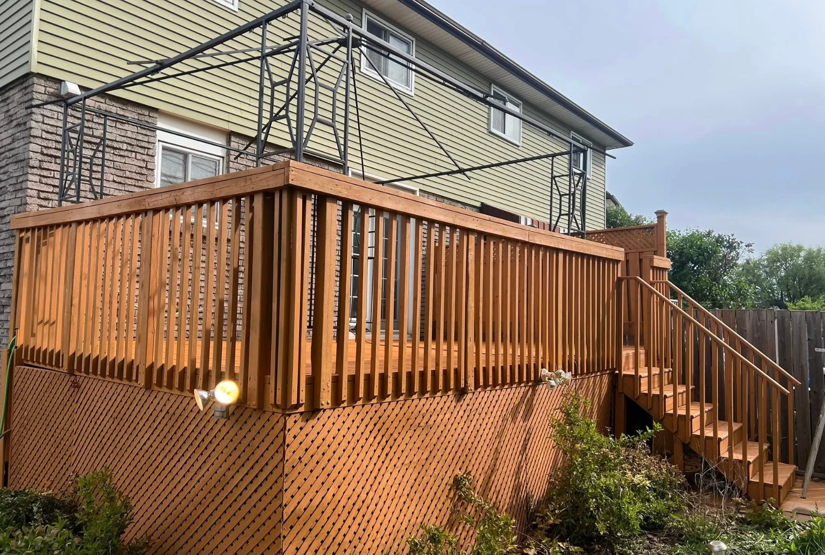 elevated-deck-staining-after-cedar-tone-houston Beautifully stained elevated deck with railings lattice and matching fence in warm cedar tone finish