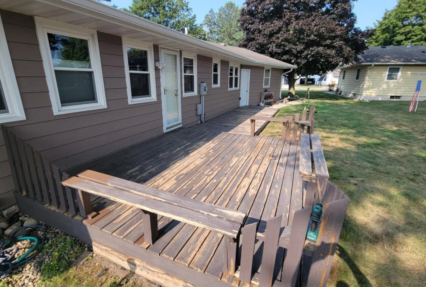 peeling-deck-stain-before-refinishing-houston Worn deck with peeling brown stain and bare wood spots on benches and railings before deck refinishing service